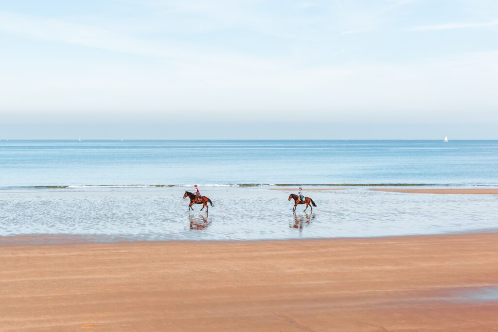 holiday goers riding horses on the beach at low tide