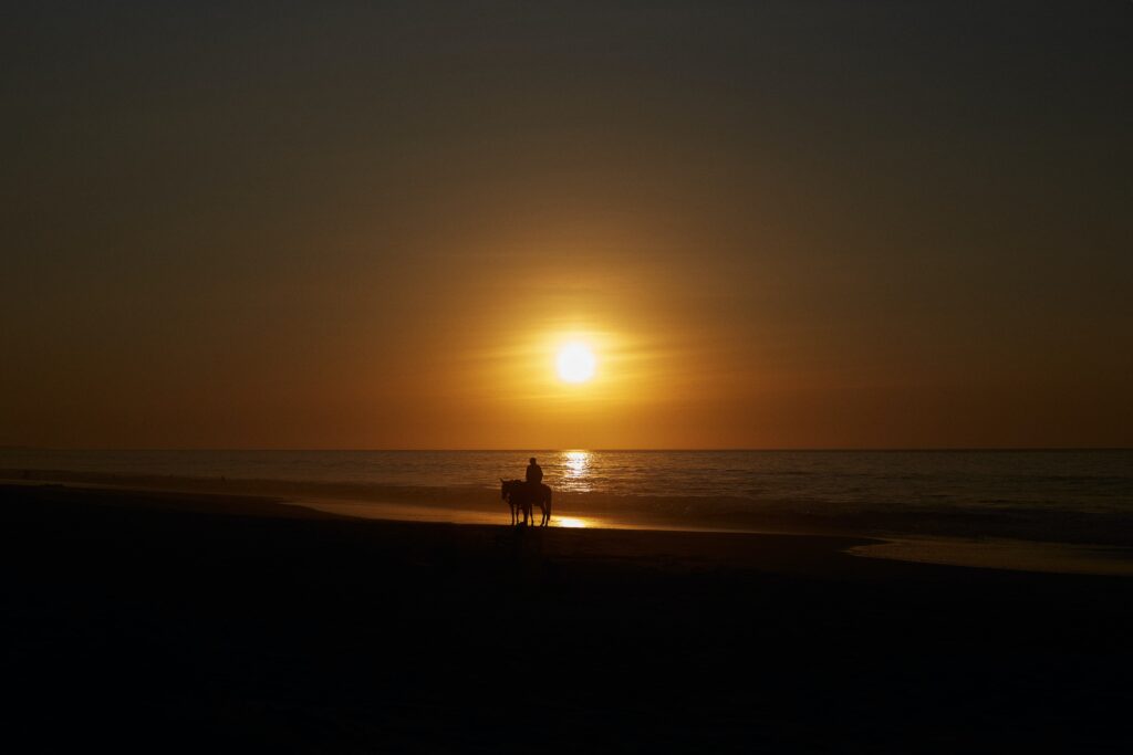 riding horses on the beach at sunset