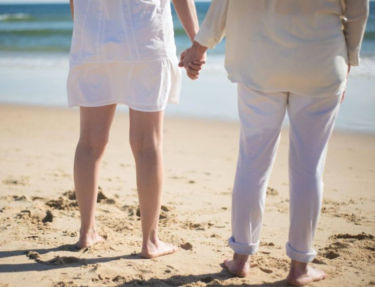  A couple holding hands while standing on a sandy beach in front of the ocean