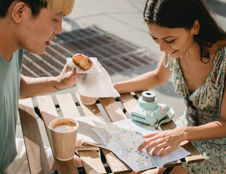 A couple pictured planning their romantic getaway with a travel map, while enjoying a coffee and a baked good