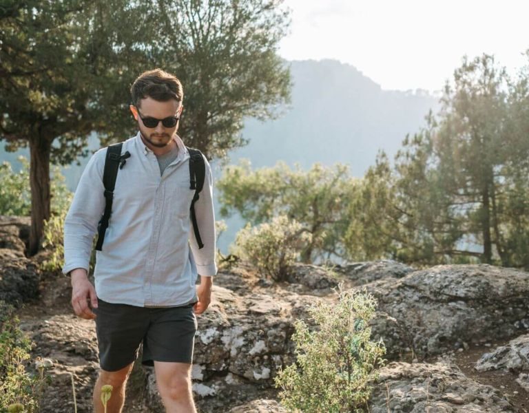 a man pictured hiking through a mountainous region on a sunny day