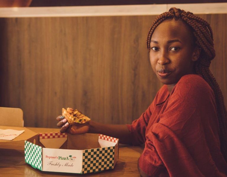 A woman eating a pizza alone, staring at the camera